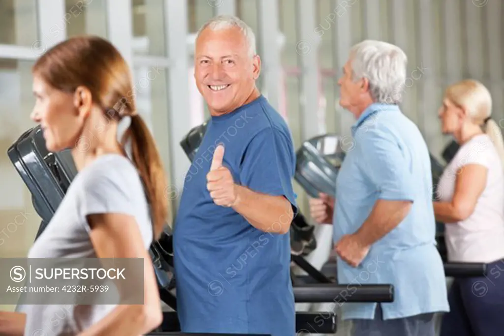 Happy senior man holding thumbs up on treadmill in gym