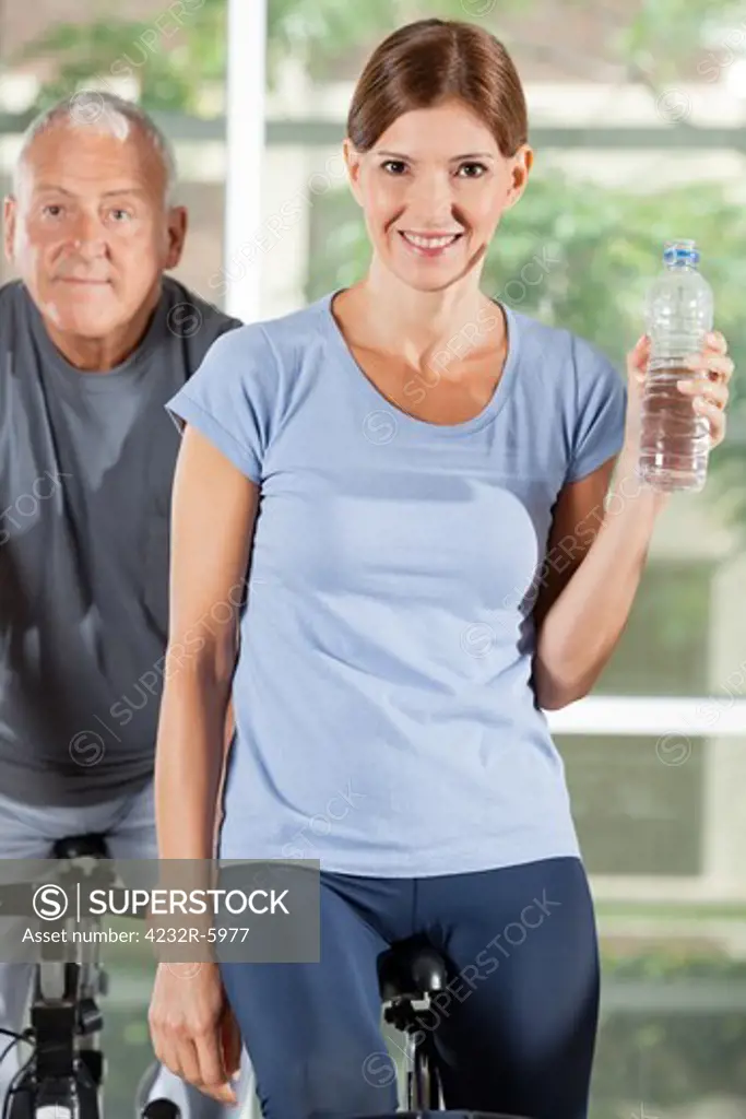 Smiling woman with water bottle on bike in fitness center