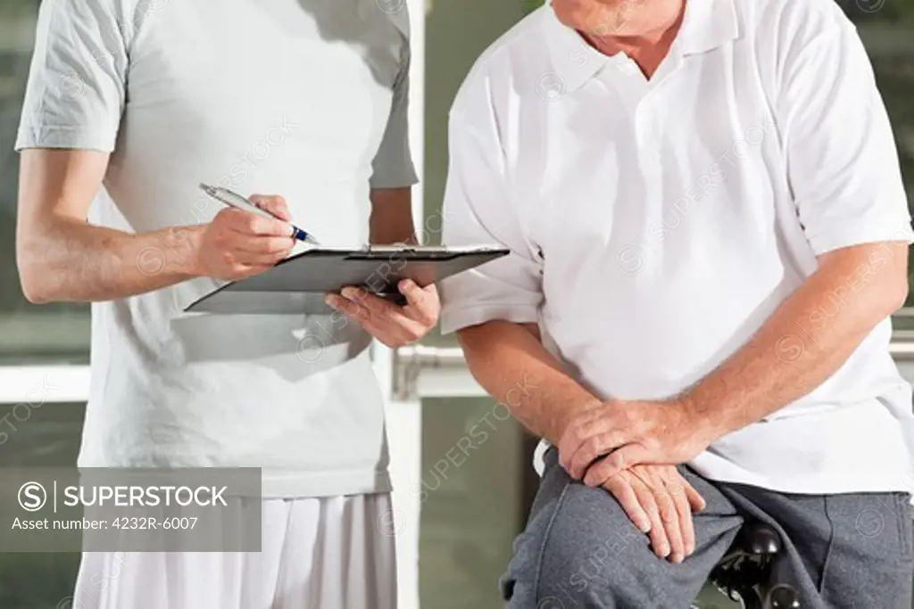 Fitness trainer in gym with clipboard creating training plan for senior man