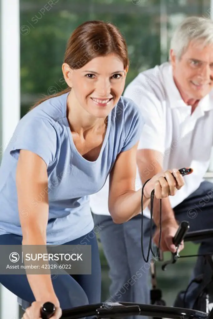 Happy woman with stopwatch in gym on spinning bike