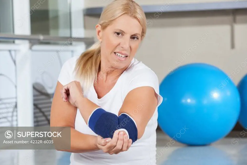 Elderly woman holding her aching elbow with bandage in gym