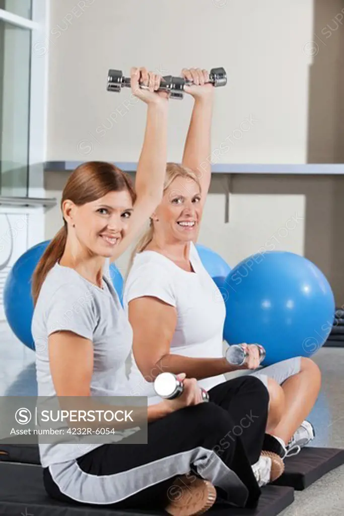 Two elderly women using dumbbells in fitness center on gym mats