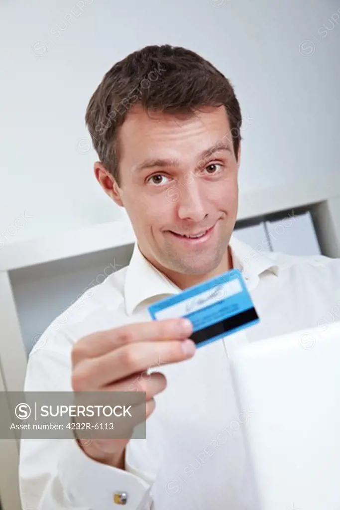 Smiling business man with laptop and credit card in office