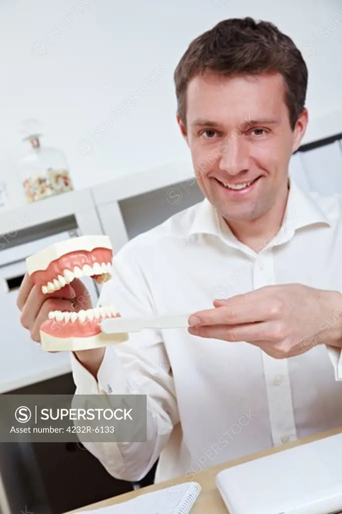 Smiling dentist in office offering tips for brushing teeth with toothbrush