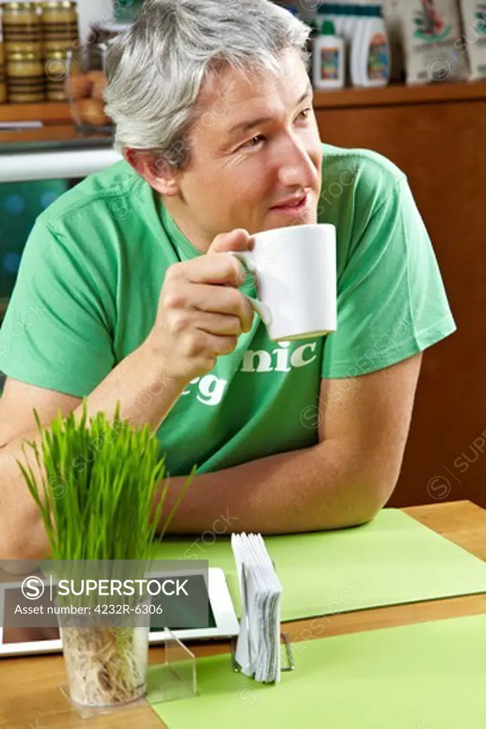 Man with tablet computer drinking cup of coffee in a caf