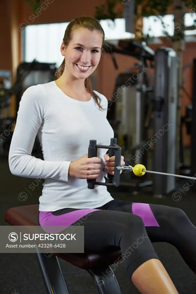 Happy woman exercising in fitness center on cable machine