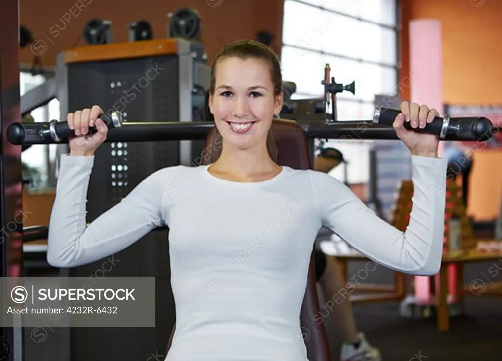 Happy young woman in sport studio exercising on a shoulder press