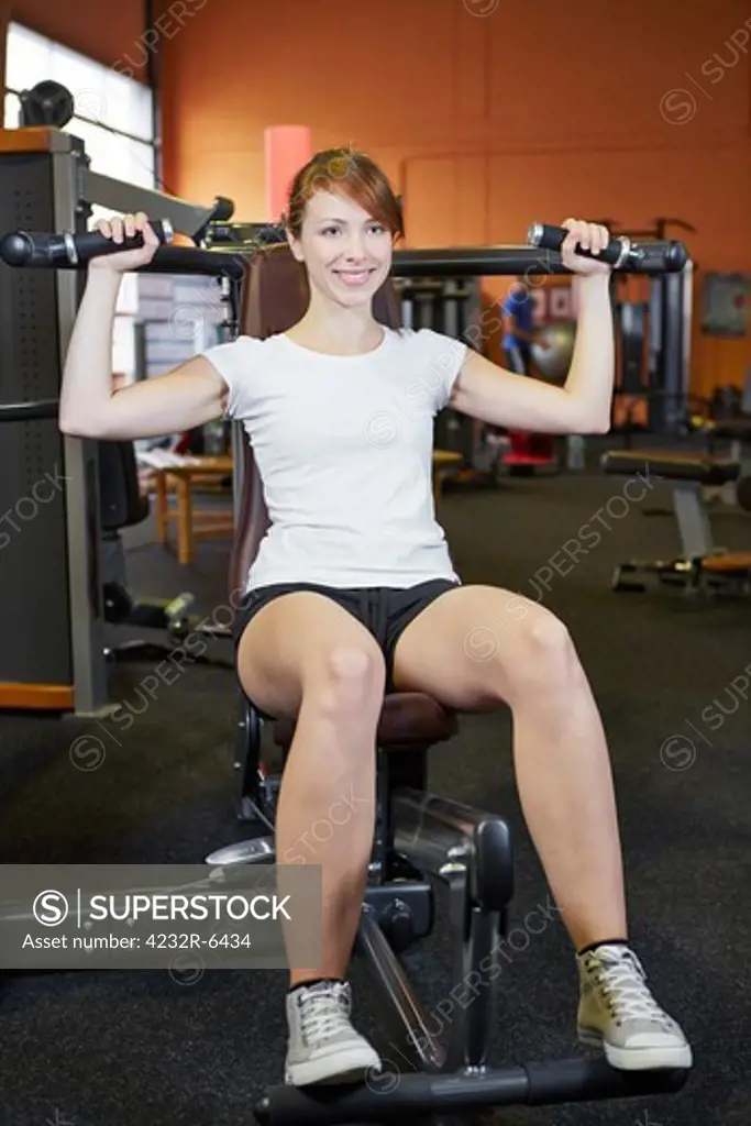 Young woman sitting on shoulder press in a fitness club