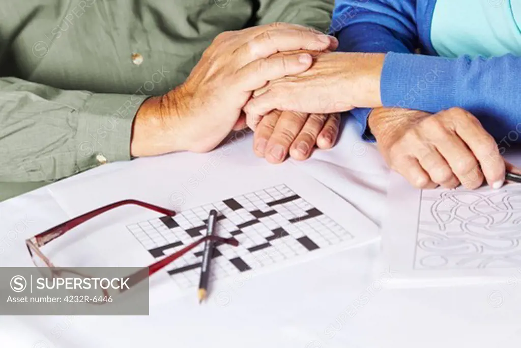 Two seniors holding their hands in a nursing home with riddles and glasses on table