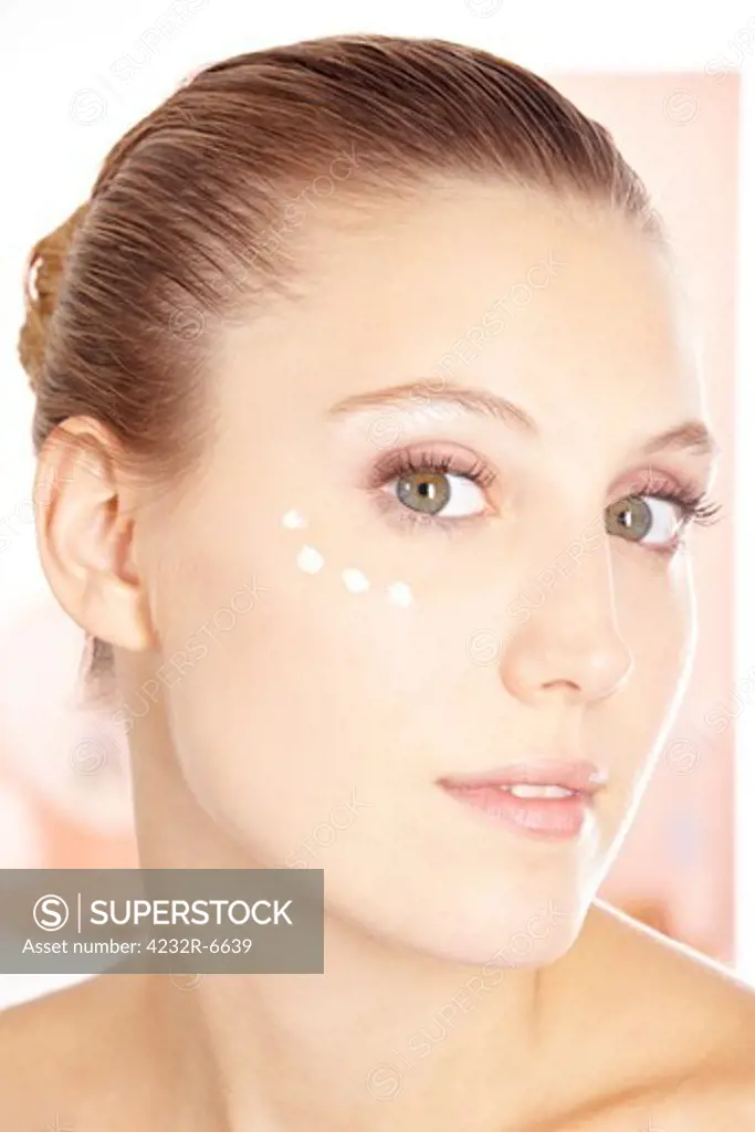 Attractive young woman with eye cream moisturizer in her face