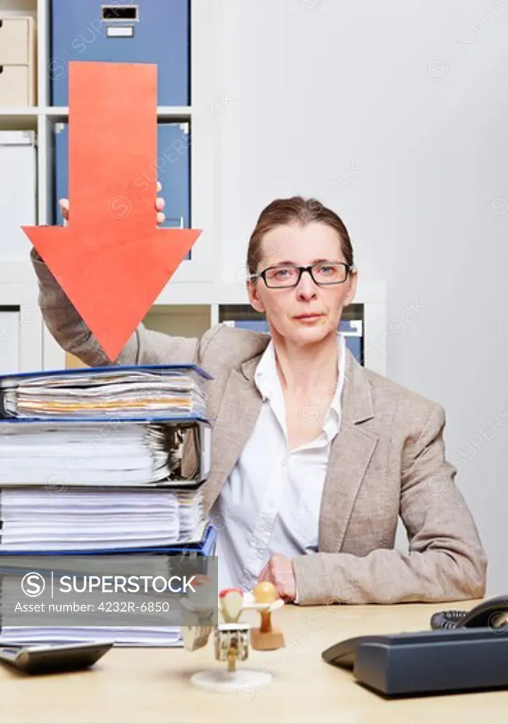 Strict business woman in her office pointing arrow to stack of files