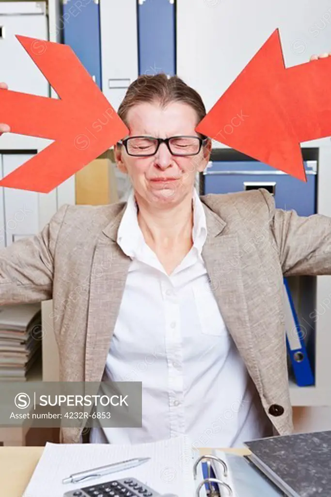 Business woman in office with headache pointing to head with red arrows