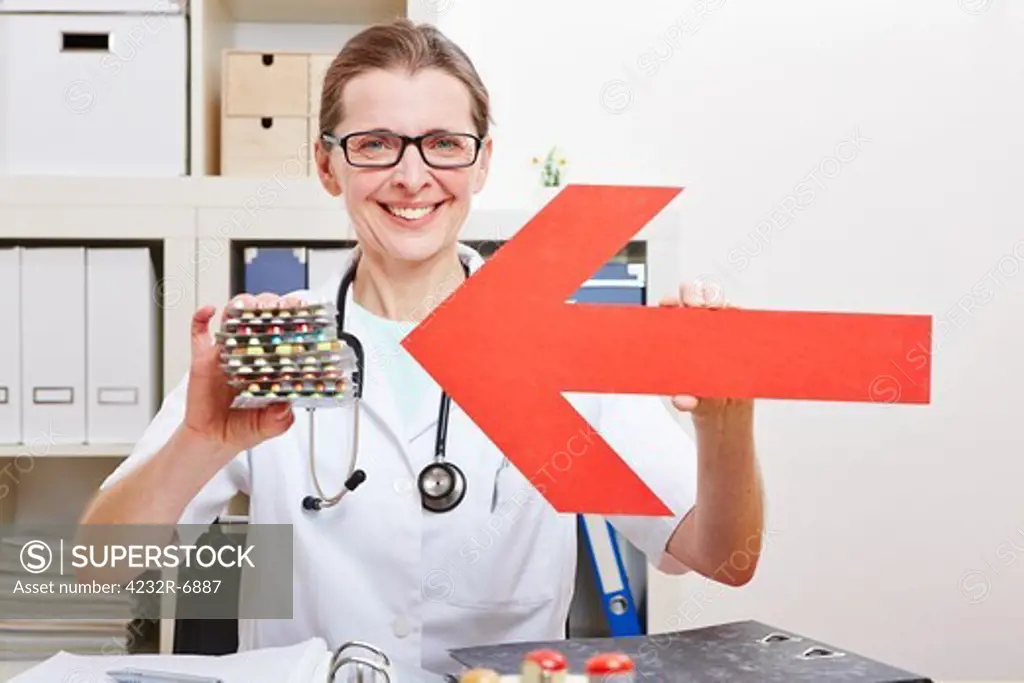 Happy female doctor pointing red arrow to medical pills in her office