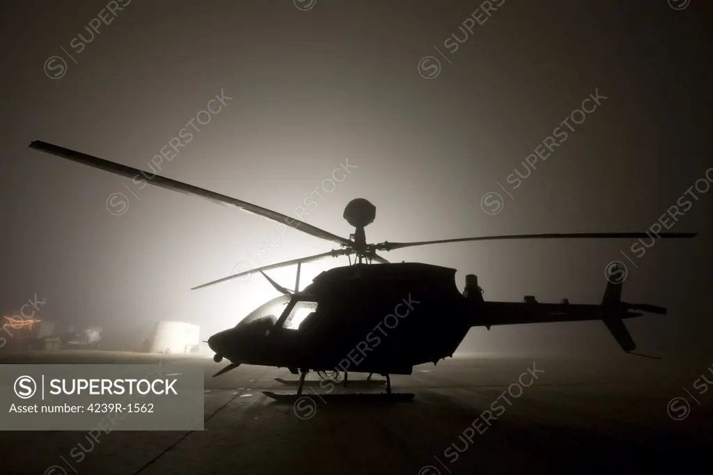 The illumination from the bright light silhouettes a OH-58D Kiowa helicopter during thick fog