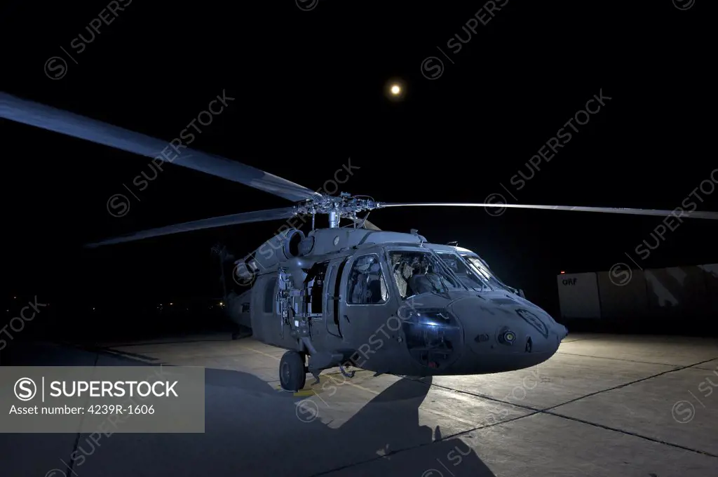 A UH-60 Black Hawk helicopter lit up by multiple flash units under a full moon