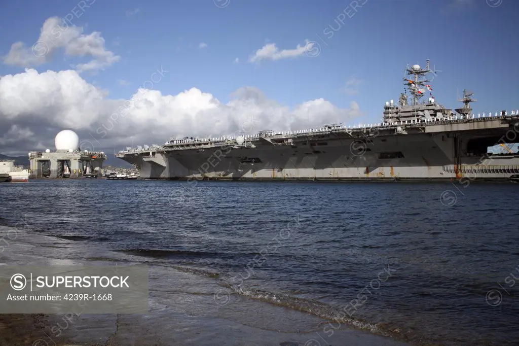 USS Abraham Lincoln (CVN-72), after participating in the multi-national exercise RIMPAC, is towed into Pearl Harbor and approaches the Sea Based X-band Radar undergoing service at the Pearl Harbor Shipyard