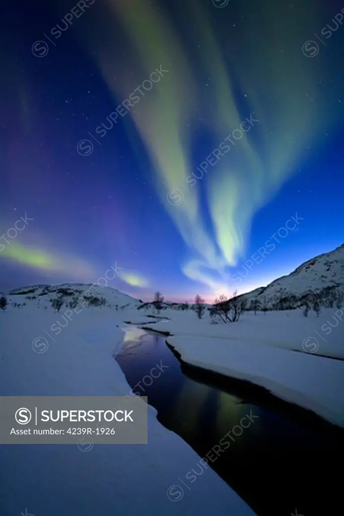 Aurora Borealis over Skittendalen Valley and the Skittendalen River in Troms County, Norway. Auroras are the result of the emissions of photons in the Earth's upper atmosphere.