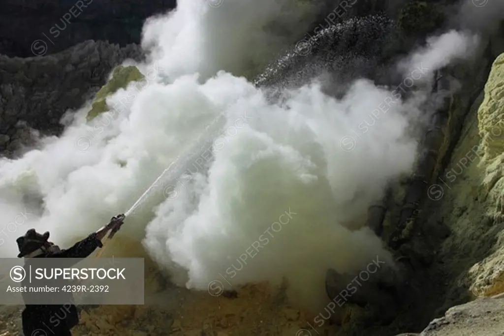 August 13, 2011 - Miner cooling condensation pipes by spraying water on them, Kawah Ijen volcano, Java, Indonesia.