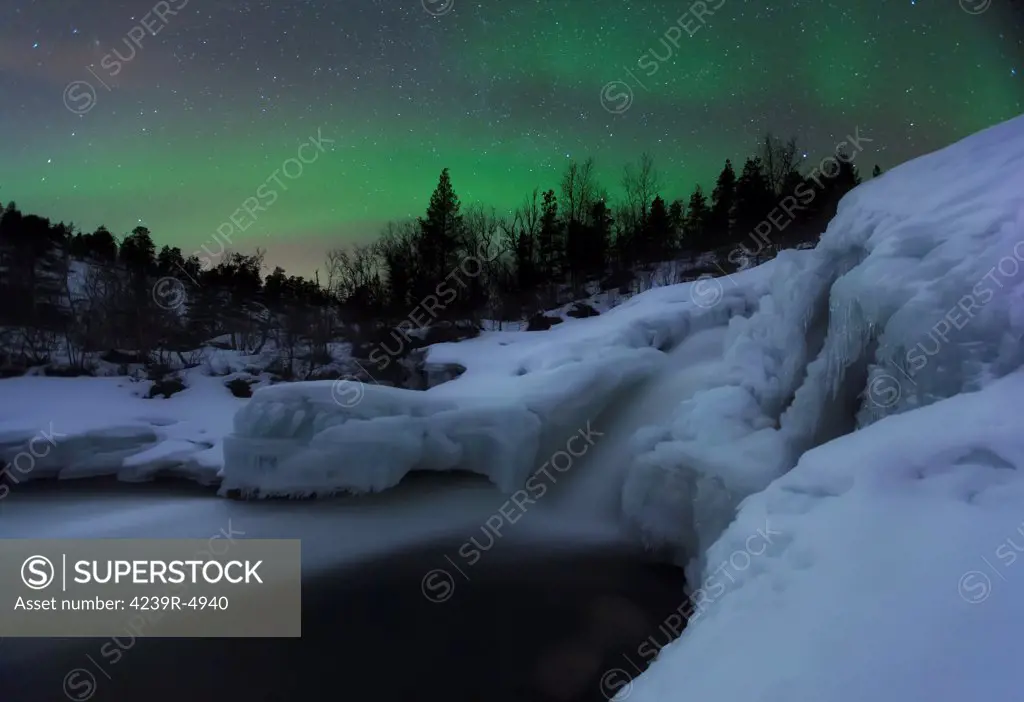 A wintery waterfall and aurora borealis over Tennevik River, Troms, Norway.