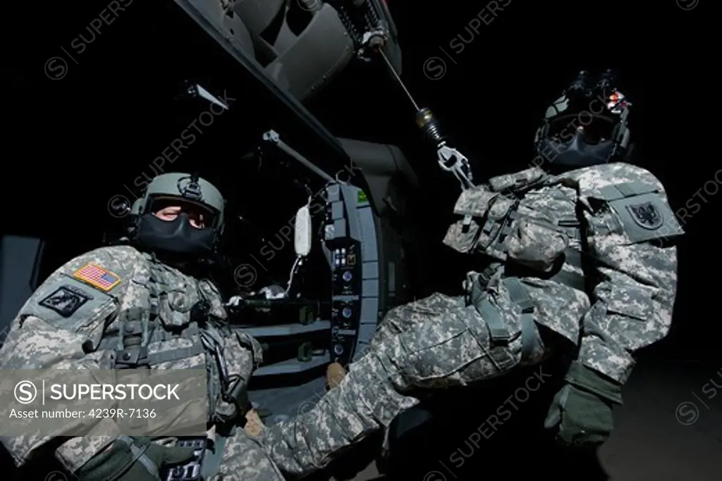 Crew Chief sits in the doorway of a UH-60 Black Hawk medevac helicopter while the medic sits on the hoist.