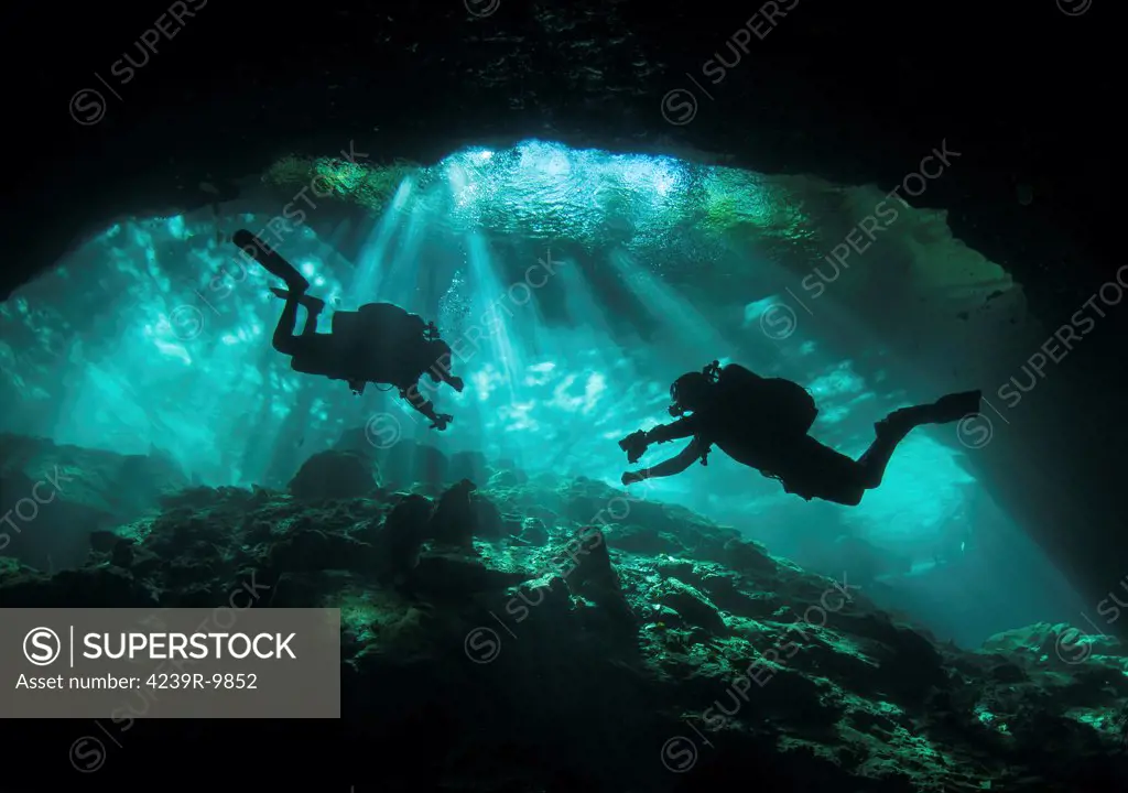 Two divers silhouetted in light at entrance to Chac Mool cenote, Mexico.