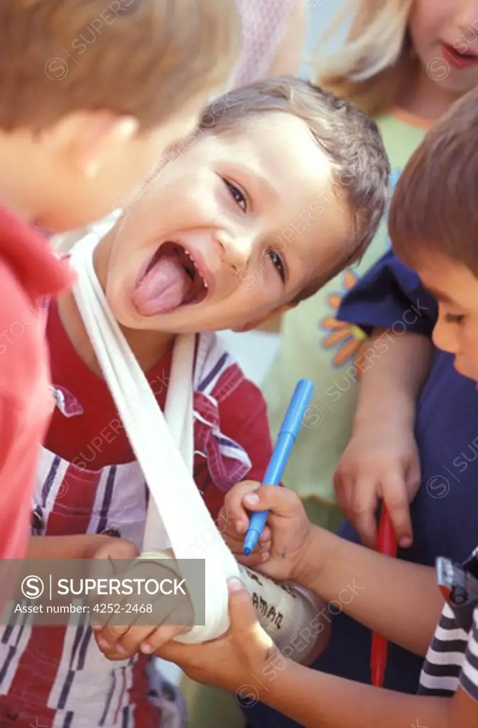 children outside boy group school arm plaster bandage pains ill wrist playtime accident wound laughing happiness writing friends comforting grimace