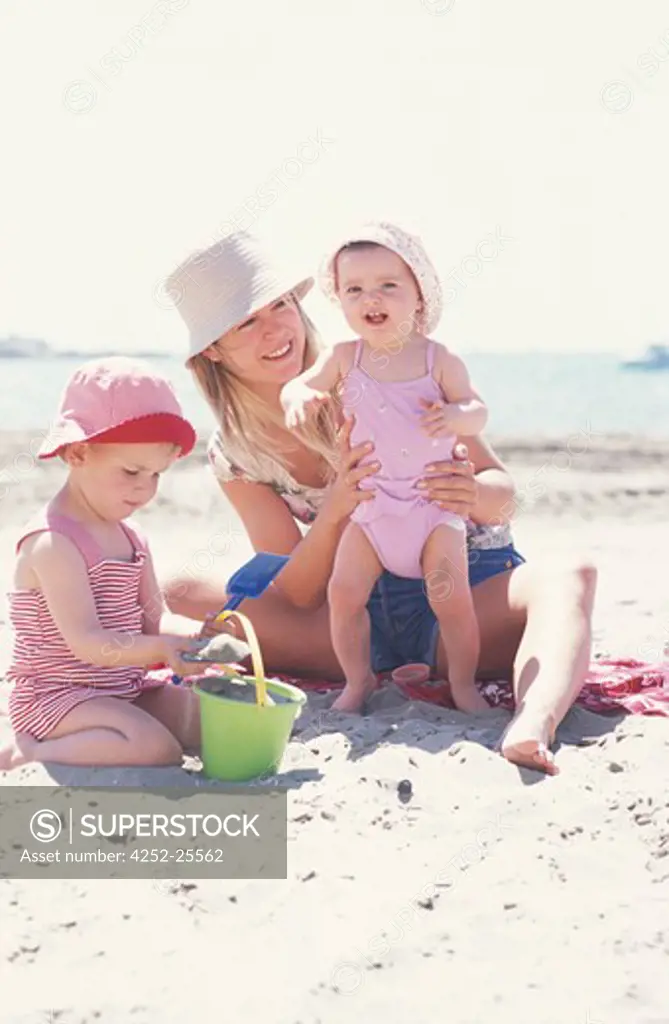 family outside girl child woman sun protection mother mummy parent summer sea beach sand sitting stand up hat swimsuit t-shirt complicity game playing toys beach accessory bucket spade smiling holidays happiness