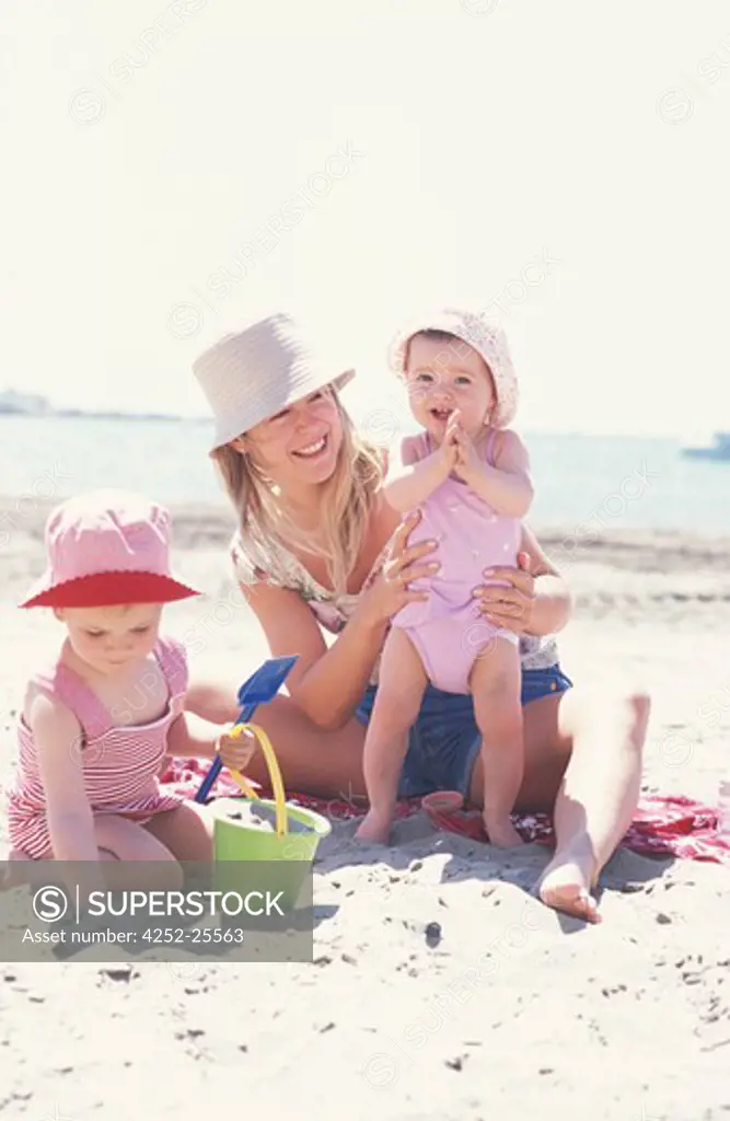 family outside girl child woman sun protection mother mummy parent summer sea beach sand sitting stand up hat swimsuit t-shirt complicity game playing toys beach accessory bucket spade movement hand applaud smiling holidays happiness