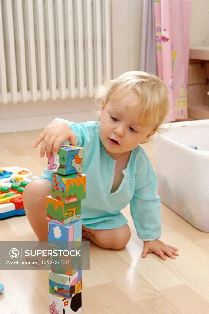 Baby girl sitting on wooden floor and playing with buildind blocks