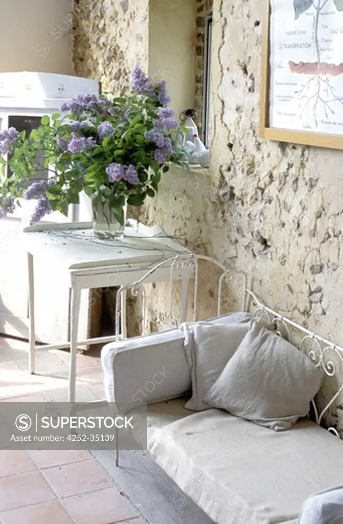 Home entrance with a small sofa and white table nearby with a large lillac flower bunch on it