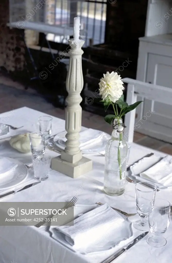 Set table into a white kitchen, candlestick and a flower into a bottle of water on it