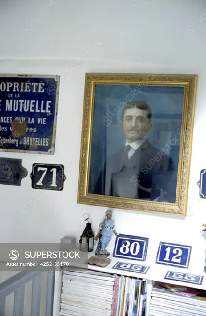 Wall decorated with a painting surrounded by a collection of blue street numbers brasses on the top of bookshelves