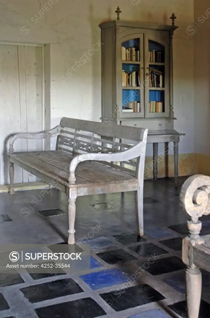 Wooden antique benches into the library room with a blue and grey tiled floor and antique bookshelf furniture in the background