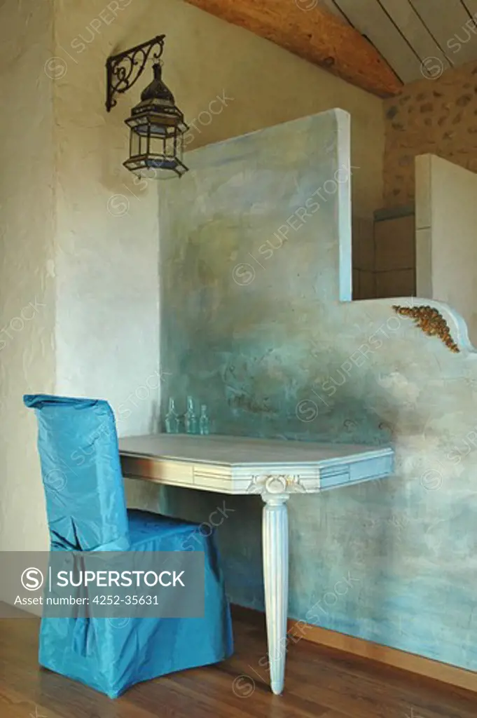 Table and chair with a blue cloth cover in front of a divinding wall painted with a blue patina into a bedroom