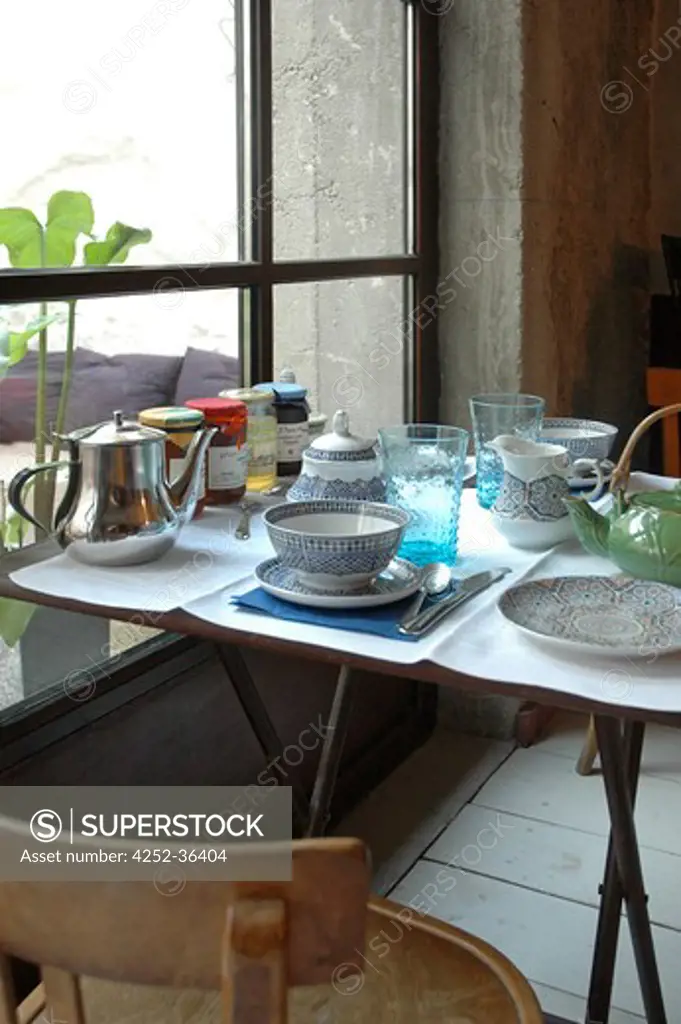 Breakfast table with teapots and jam near a window