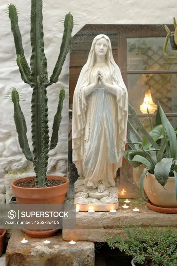 Religious statue with candles around and potted cactuses