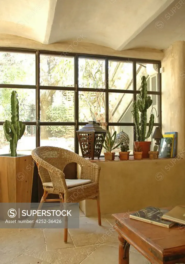 Wicker chair behing a large window and potted cactuses behind