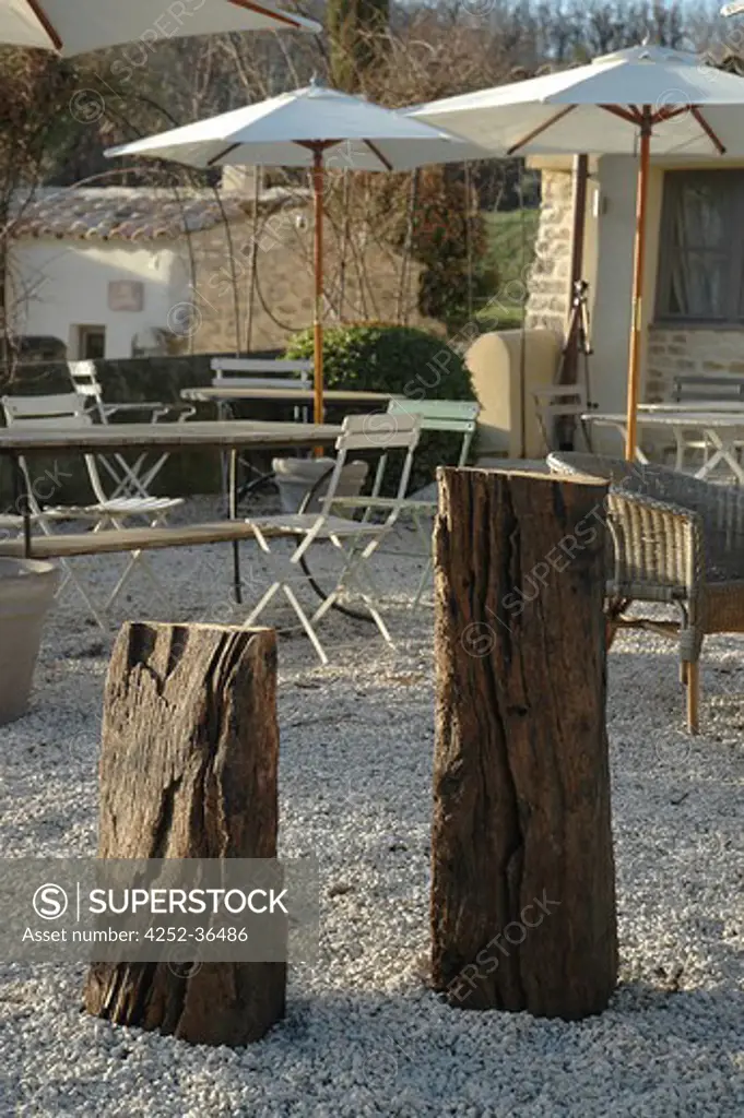 Raw wood pieces on a gravel terrace with tables, benches and sunshades