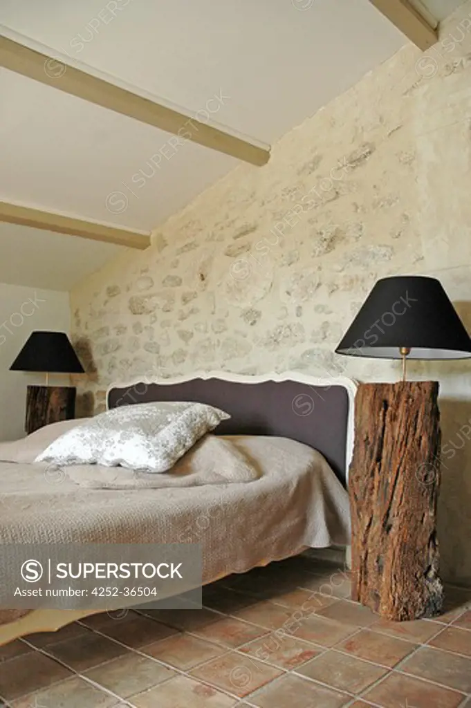 Attic bedroom with stone wall, tiled floor, bed with a classic bedhead and bedsides made with raw wood logs