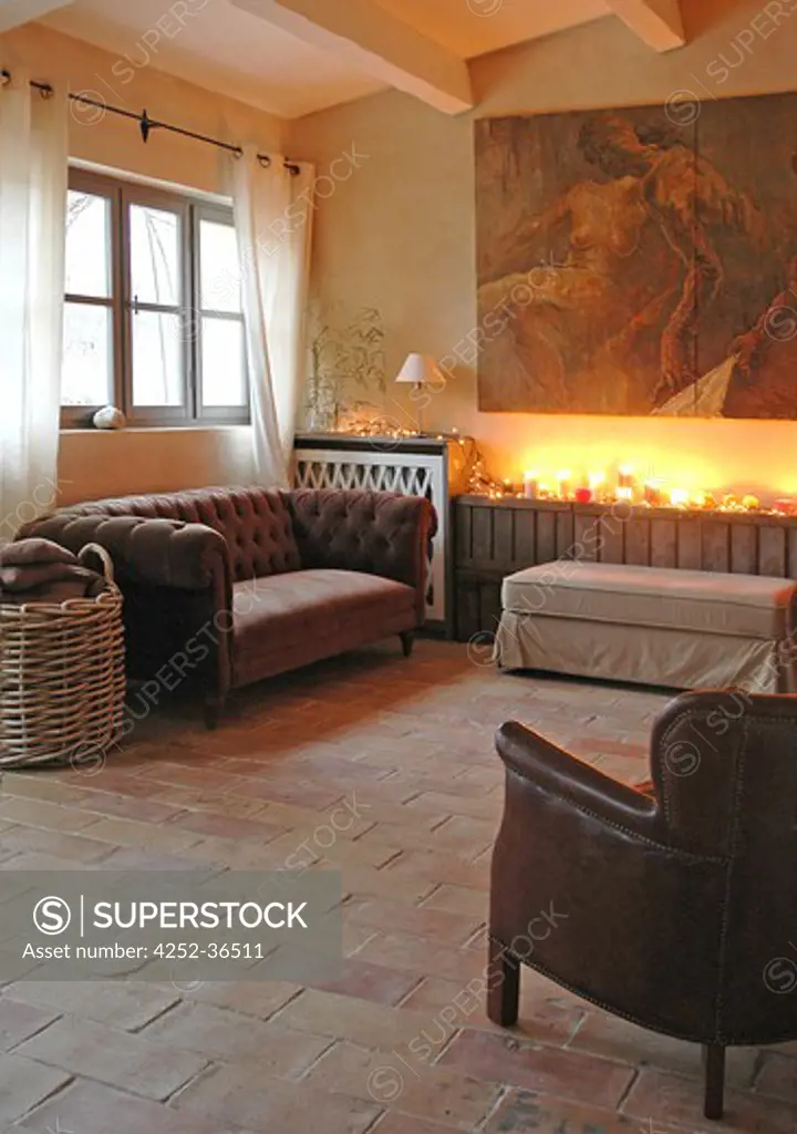 Brown sofa, leather armchair and large painting into a living room with a tiled floor