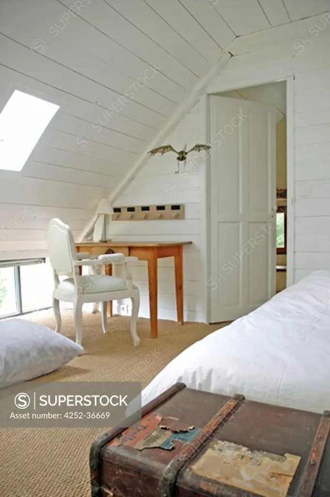White attic bedroom with a bed and an old bargain hunt suitcase, sisal covered floor