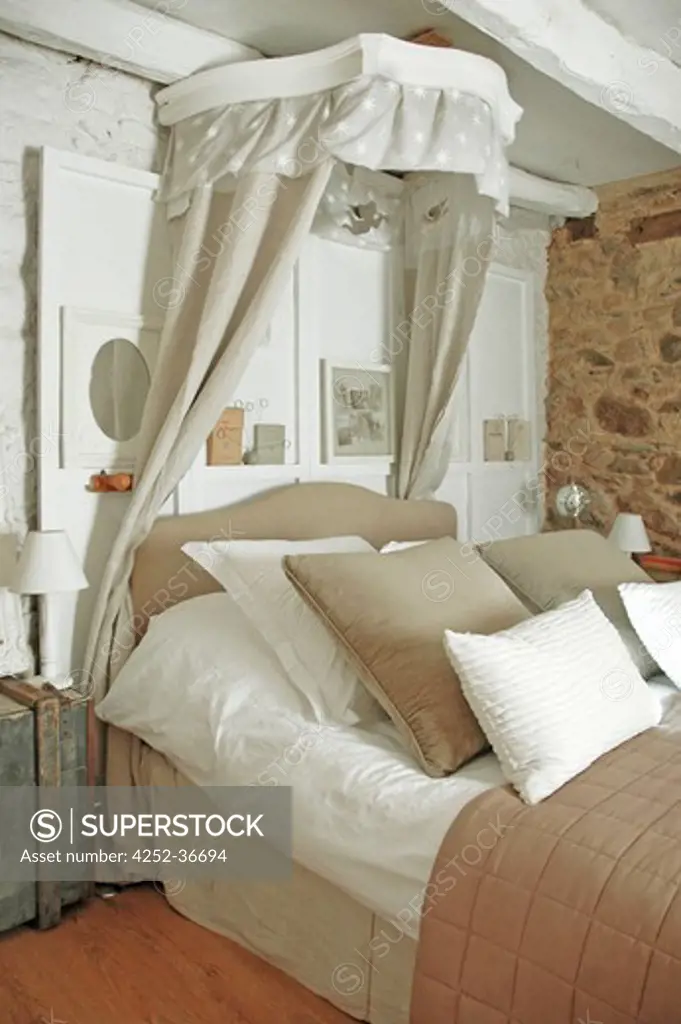 Old style bedroom with a beige bed, curtains above covered with cushions and pillows