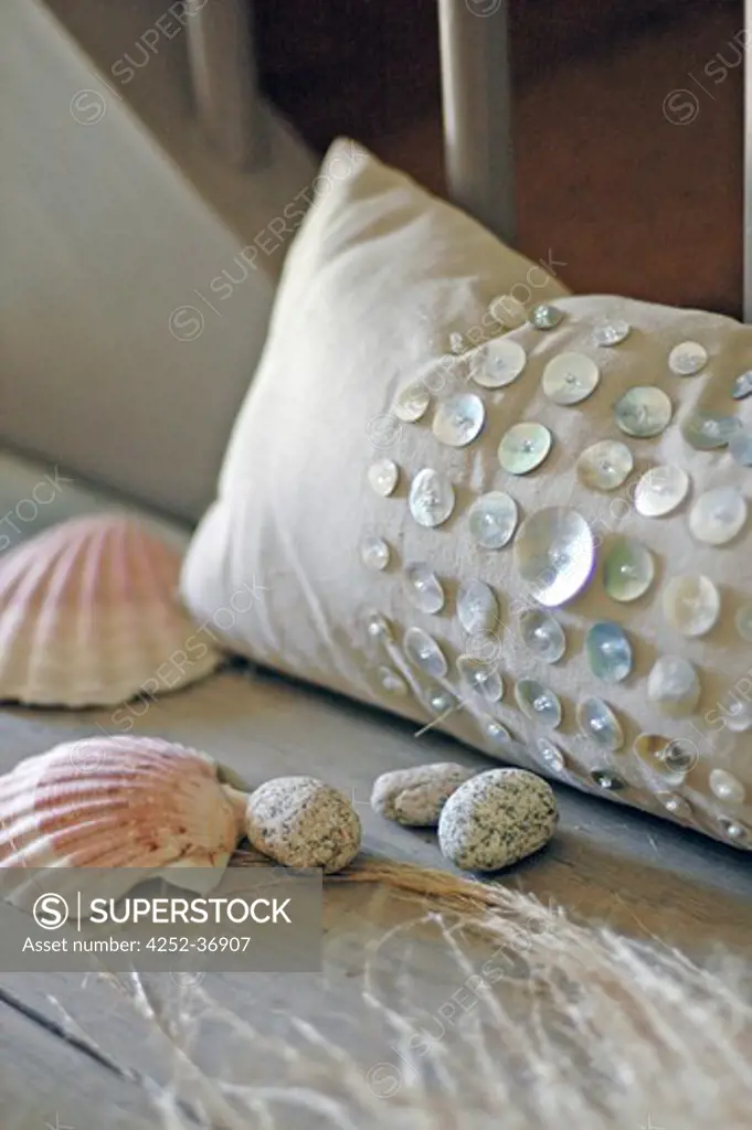 Beige cushion with pearly buttons, shells and pebbles nearby