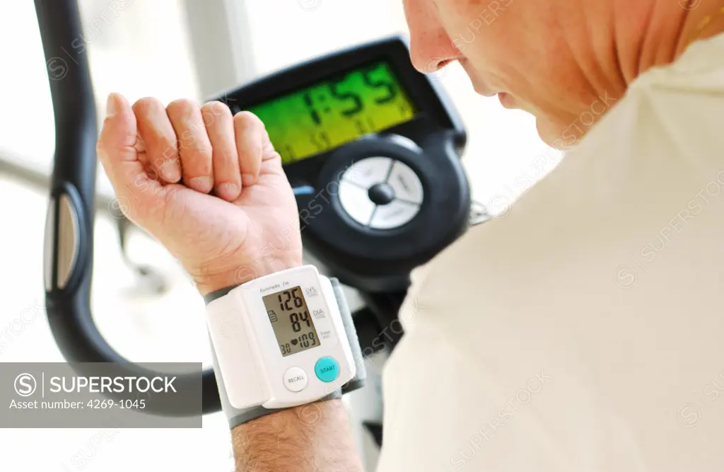 Man monitoring his blood pressure with a portable digital sphygmomanometer when practising excercize bicycle.