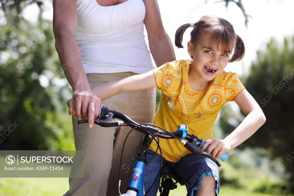 7 years old girl learning to ride a bicycle with her mother.