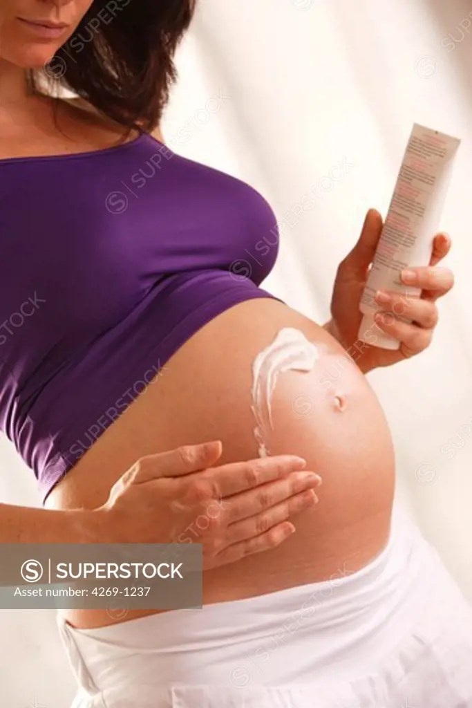 Pregnant woman rubbing cream into her swollen abdomen. Keeping skin supple by moisturizing helps to diminish stretch marks.