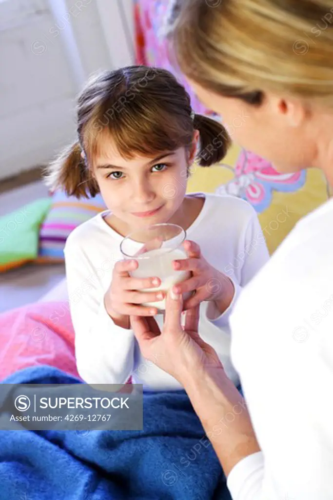 7 years old girl drinking a glass of milk in bed.