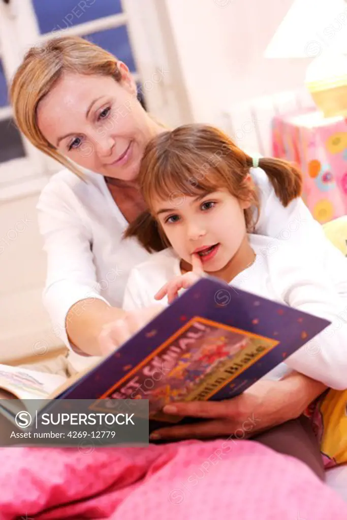 Mother reading a book to her 7 years old daughter.