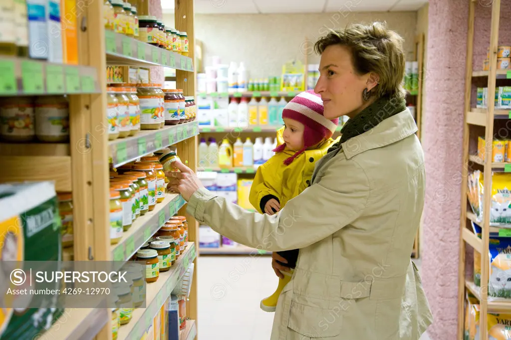 Mother with her 12 months old baby shopping for baby food in organic supermarket.
