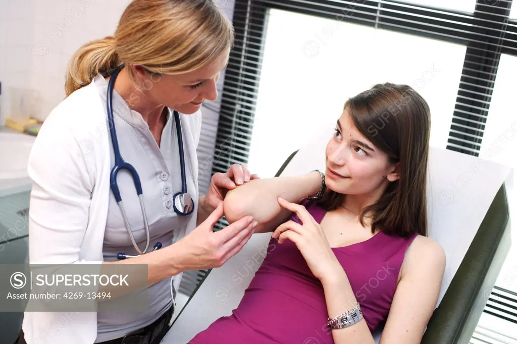 Doctor examining the skin of a teenage patient.